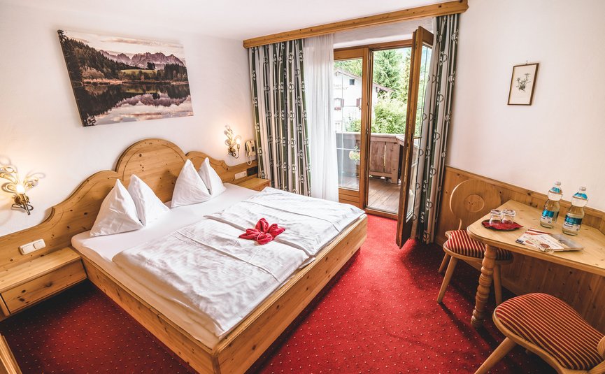 Gemütliches Hotelzimmer mit Holzmöbeln, rotem Teppich und Balkon mit Aussicht