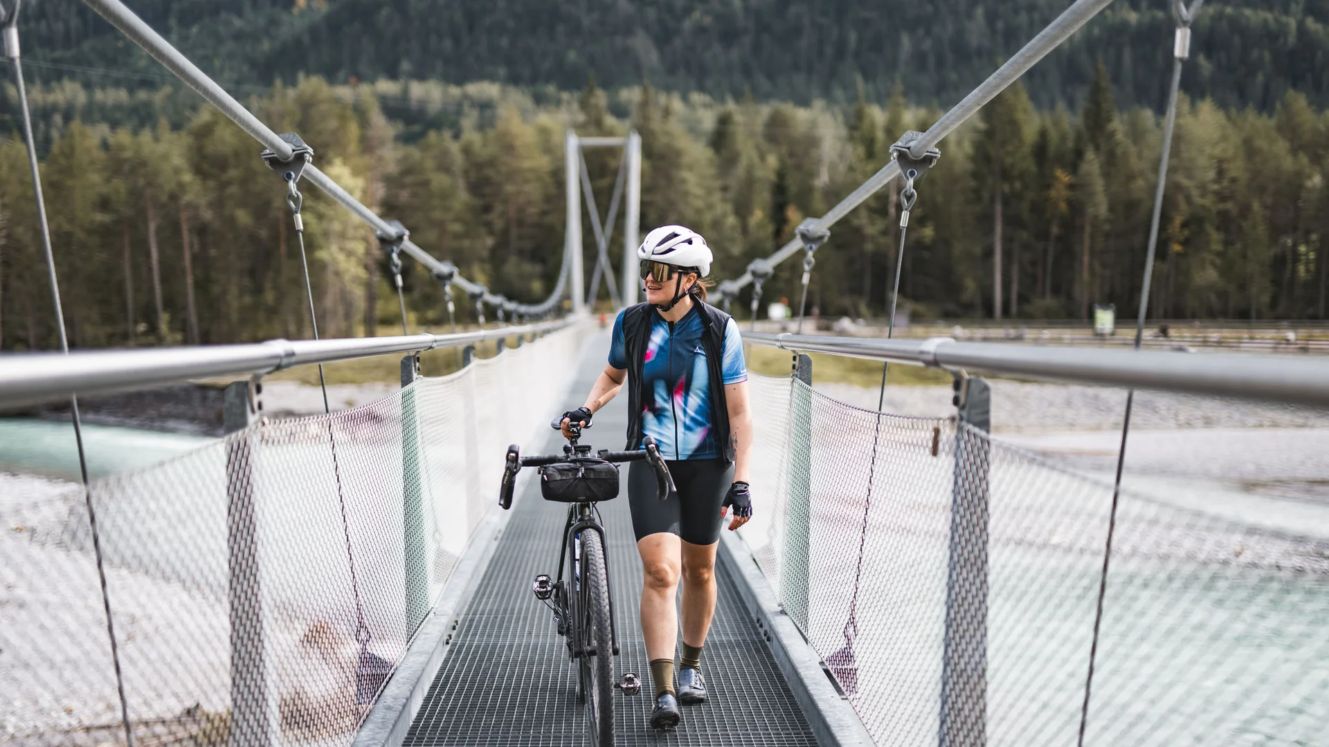 Radfahrer geht mit Rennrad über eine Hängebrücke in den Bergen