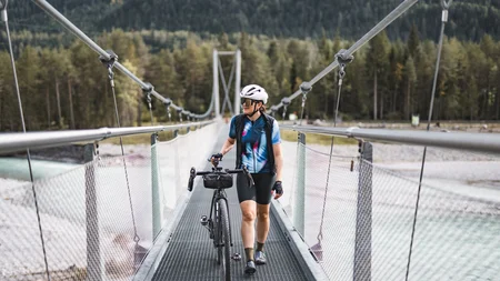 Cyclist walking bike across a suspension bridge in the mountains