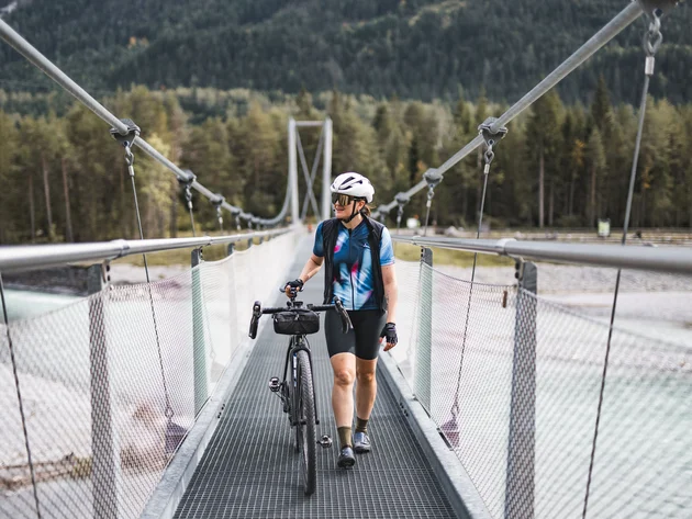 Cyclist walking bike across a suspension bridge in the mountains