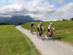 Brixental © Michael Küchl Drei Radfahrer auf Landstraße mit Bergen und Wolken im Hintergrund