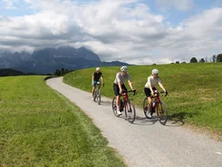 Three cyclists on country road with mountains and clouds behind