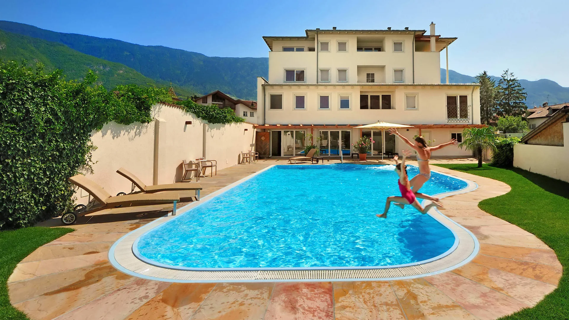 Auf Schotterkurs im Hotel Teutschhaus © Hotel Teutschhaus Kurtinig Zwei Kinder springen im Pool eines Hauses mit Bergblick