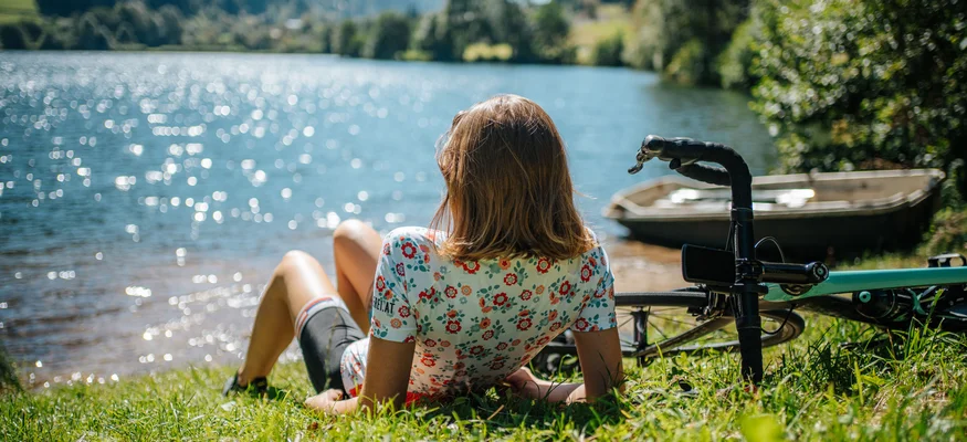 Woman relaxing by lake with bike, scenic water and mountain view
