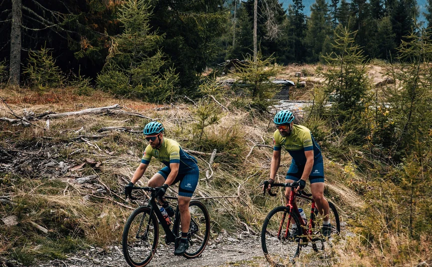 Zwei Radfahrer auf gravel Fahrrädern in bergigem Waldgebiet bei bewölktem Himmel