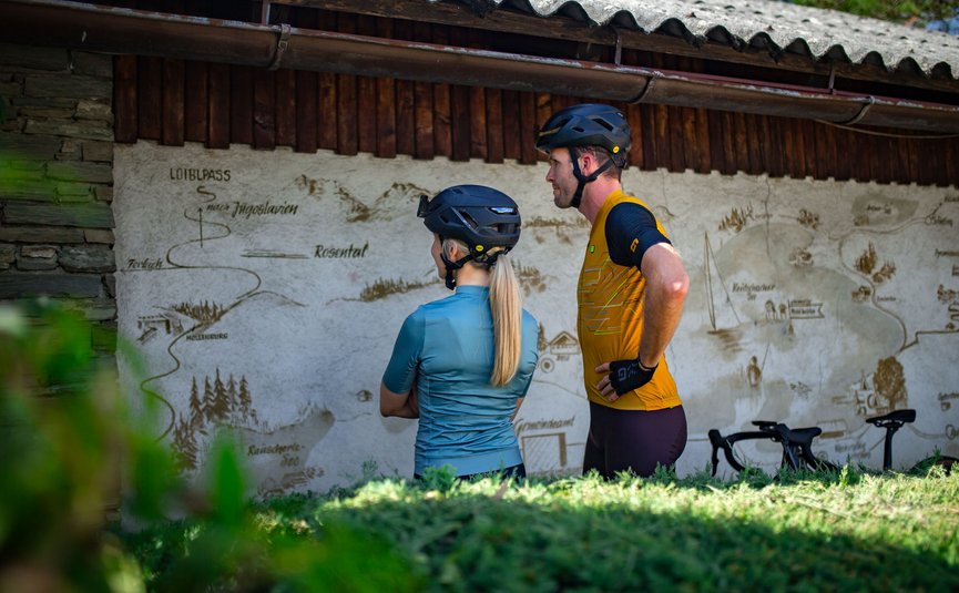 Gravel bike holiday on Lake Wörthersee © Nicola Littmann Two cyclists wearing helmets looking at a map on a wooden building wall