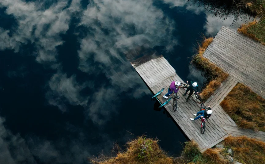Gravelbike Urlaub in der NOCKBIKE Area © Martin Hofmann Drei Radfahrer auf einem Steg am See mit Wolkenreflektion im Wasser