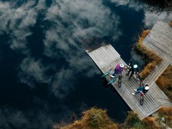 NOCKBIKE Area © Martin Hofmann Drei Radfahrer auf einem Steg am See mit Wolkenreflektion im Wasser