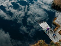 NOCKBIKE Area © Martin Hofmann Drei Radfahrer auf einem Steg am See mit Wolkenreflektion im Wasser