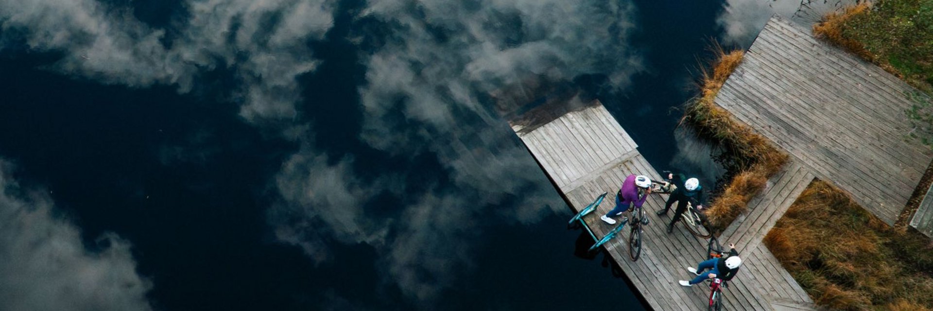 Bike Boutique Hotel Lindenhof **** © Martin Hofmann Drei Radfahrer auf einem Steg am See mit Wolkenreflektion im Wasser
