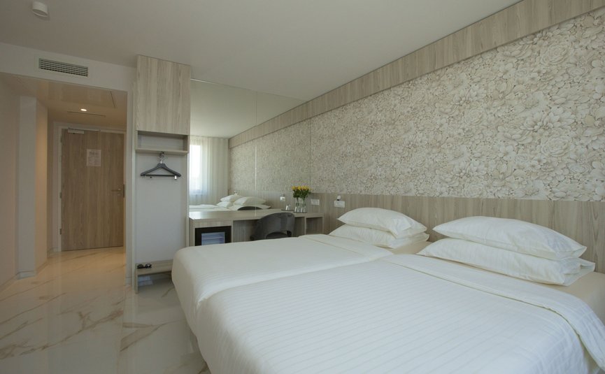 Helles Hotelzimmer mit zwei Einzelbetten und floralem Wandmuster