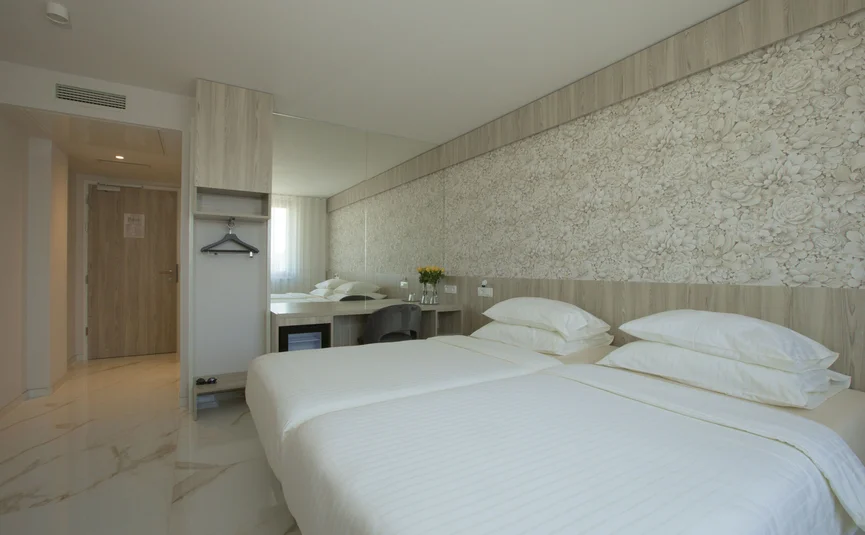 Helles Hotelzimmer mit zwei Einzelbetten und floralem Wandmuster