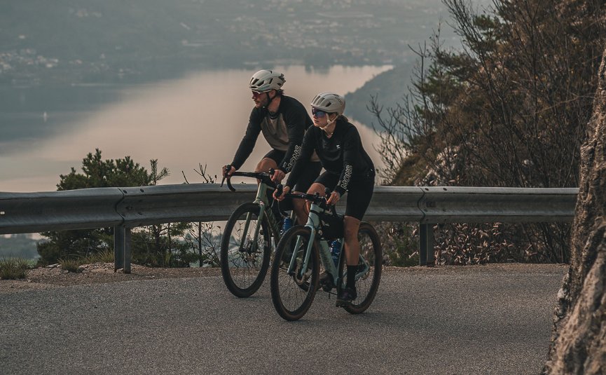 Two cyclists riding on mountain road with lake and mountains in background