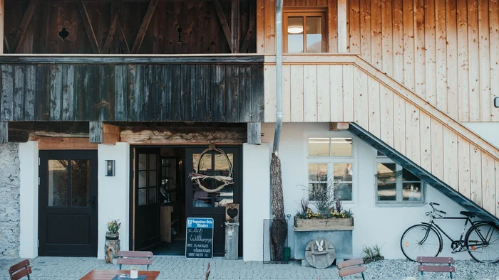 5 Tipps fürs Graveln in Oberbayern © Elisabeth Kellerer Eingang eines traditionellen Gasthauses mit Holzverkleidung und Sitzgelegenheiten außen