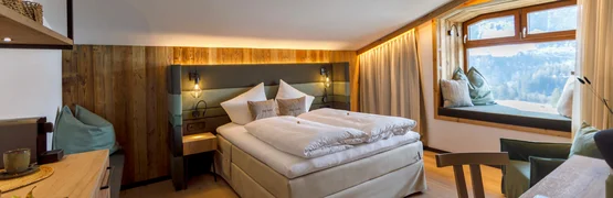 Gemütliches Hotelzimmer mit Doppelbett, Holzmöbeln und Fensterbank mit Bergblick