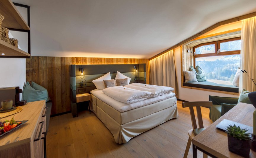 Gemütliches Hotelzimmer mit Doppelbett, Holzmöbeln und Fensterbank mit Bergblick