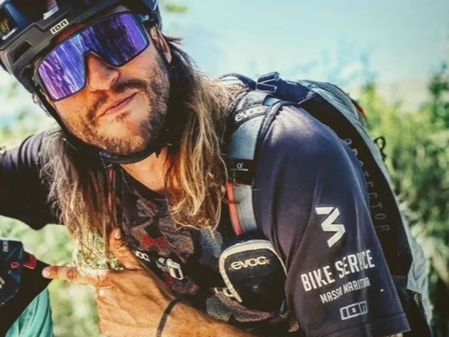 Gravelbiken in der Toskana © Tenuta il Cicalino Mann mit Fahrradhelm und Sonnenbrille zeigt nach links und trägt Rucksack