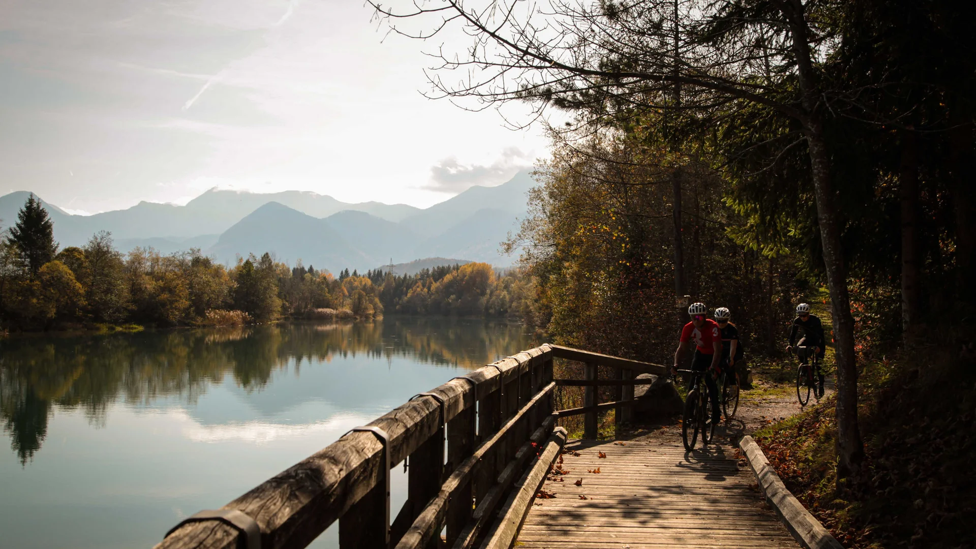 Graveln für Anfänger © Wörthersee Tourismus GmbH - Christian Riedel Radfahrer fahren auf einem Holzsteg neben einem See mit Bergen im Hintergrund