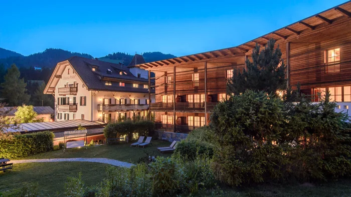 Gravel & Genuss am Kronplatz © Watzek Photografie Beleuchtete Hotelgebäude und Garten bei Dämmerung in den Bergen