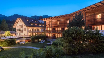 Lit hotel buildings and garden at dusk in mountain landscape