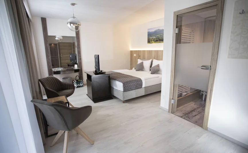 Modern hotel room with double bed, TV, and two armchairs