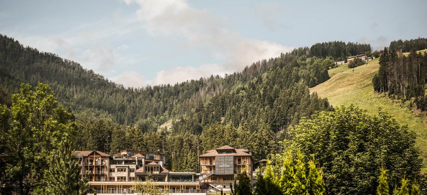 Hotelgebäude eingebettet in grüne Berge und Wald unter blauem Himmel