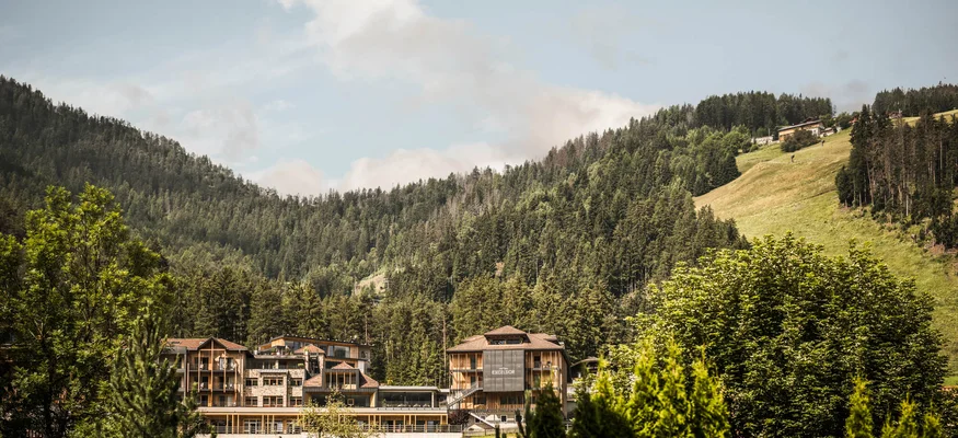 Hotelgebäude eingebettet in grüne Berge und Wald unter blauem Himmel