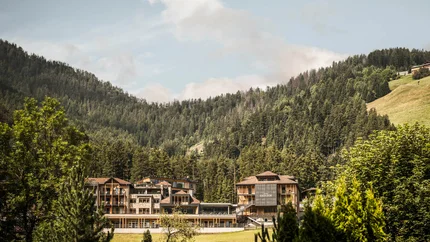 Hotelgebäude eingebettet in grüne Berge und Wald unter blauem Himmel