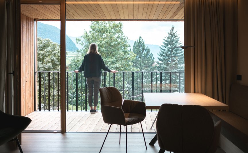 Gisse Zwölf **** © Lunah Photography - Lukas Haberer & Hannah Beikircher Person blickt vom Balkon eines Holzhauses auf grüne Bäume und Berge