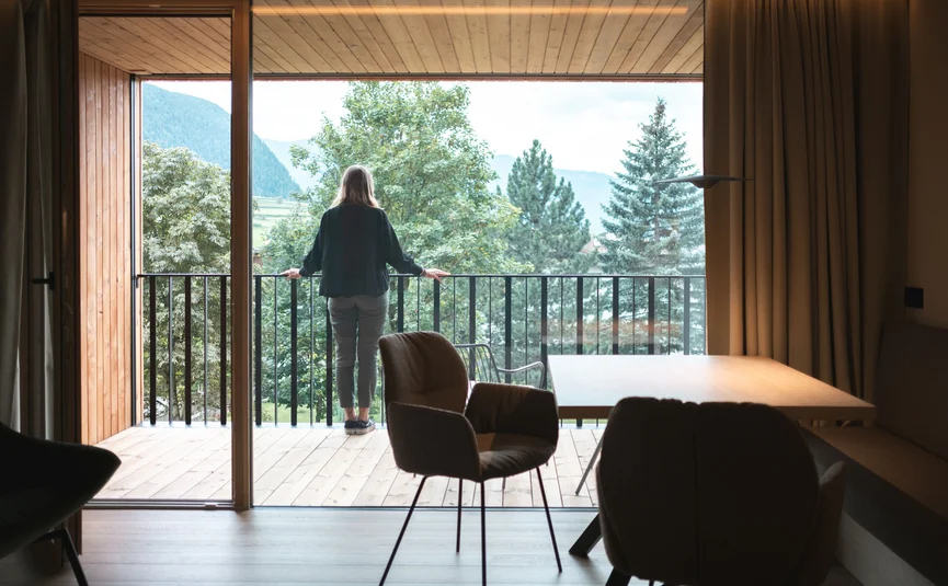 Person standing on wooden balcony looking at trees and mountains