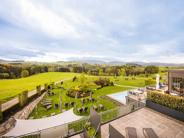 Blick auf eine Hotelterrasse mit Garten, Liegestühlen und grüner Landschaft