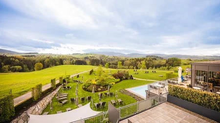 Blick auf eine Hotelterrasse mit Garten, Liegestühlen und grüner Landschaft