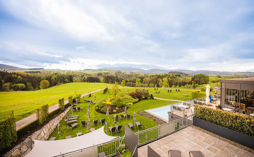 Blick auf eine Hotelterrasse mit Garten, Liegestühlen und grüner Landschaft