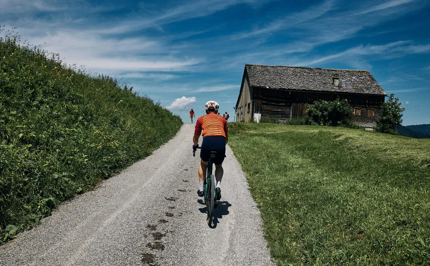 Radfahrer in rotem Trikot auf Landstraße vor Bauernhaus
