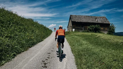 Radfahrer in rotem Trikot auf Landstraße vor Bauernhaus
