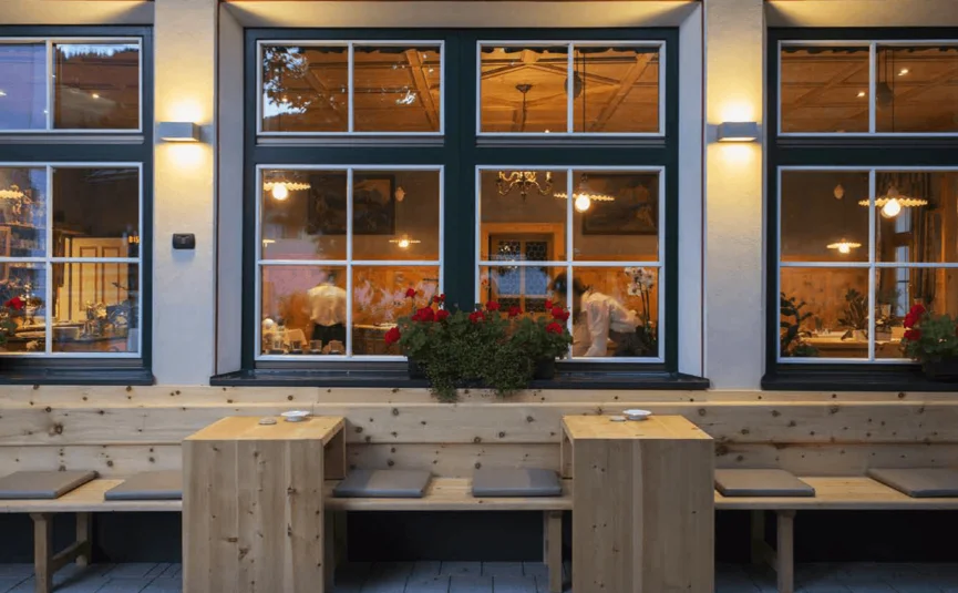 Außenansicht eines Restaurants mit Holztischen und Sitzbänken am Abend