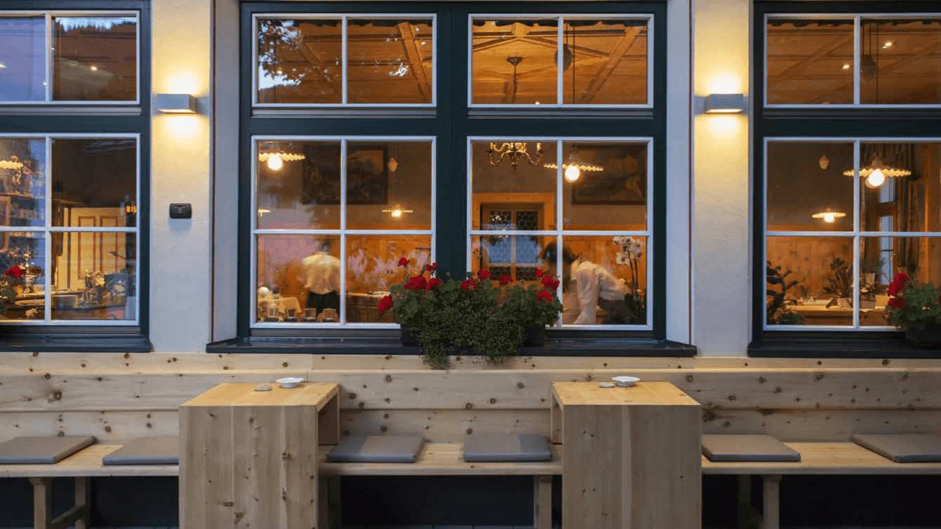 Gravel & Genuss am Kronplatz © Hotel Ostaria Posta Außenansicht eines Restaurants mit Holztischen und Sitzbänken am Abend