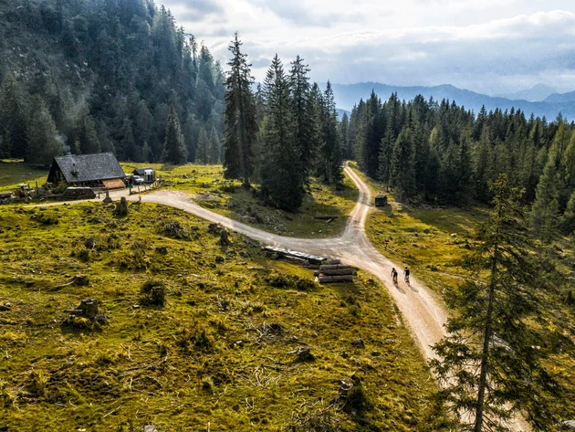 Zwei Radfahrer auf Weg in bewaldeter Berglandschaft mit Hütte