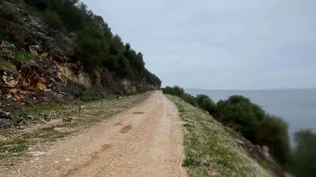 Bikepacking von Wien nach Athen © Jan Koller Schmaler Weg am Hang mit Blick auf Meer unter bewölktem Himmel