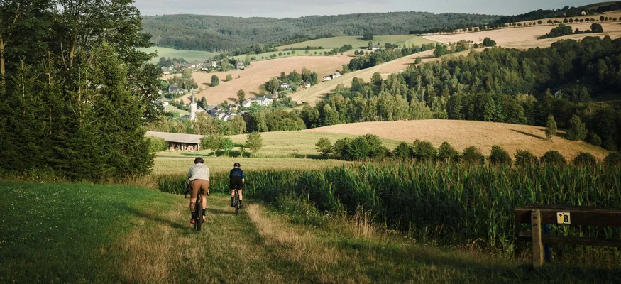 BLOCKLINE erleben im Erzgebirge © TV Erzgebirge e.V./ Lifecycle Martin Donat Zwei Radfahrer auf einem Feldweg mit Blick auf hügelige Landschaft und ein Dorf