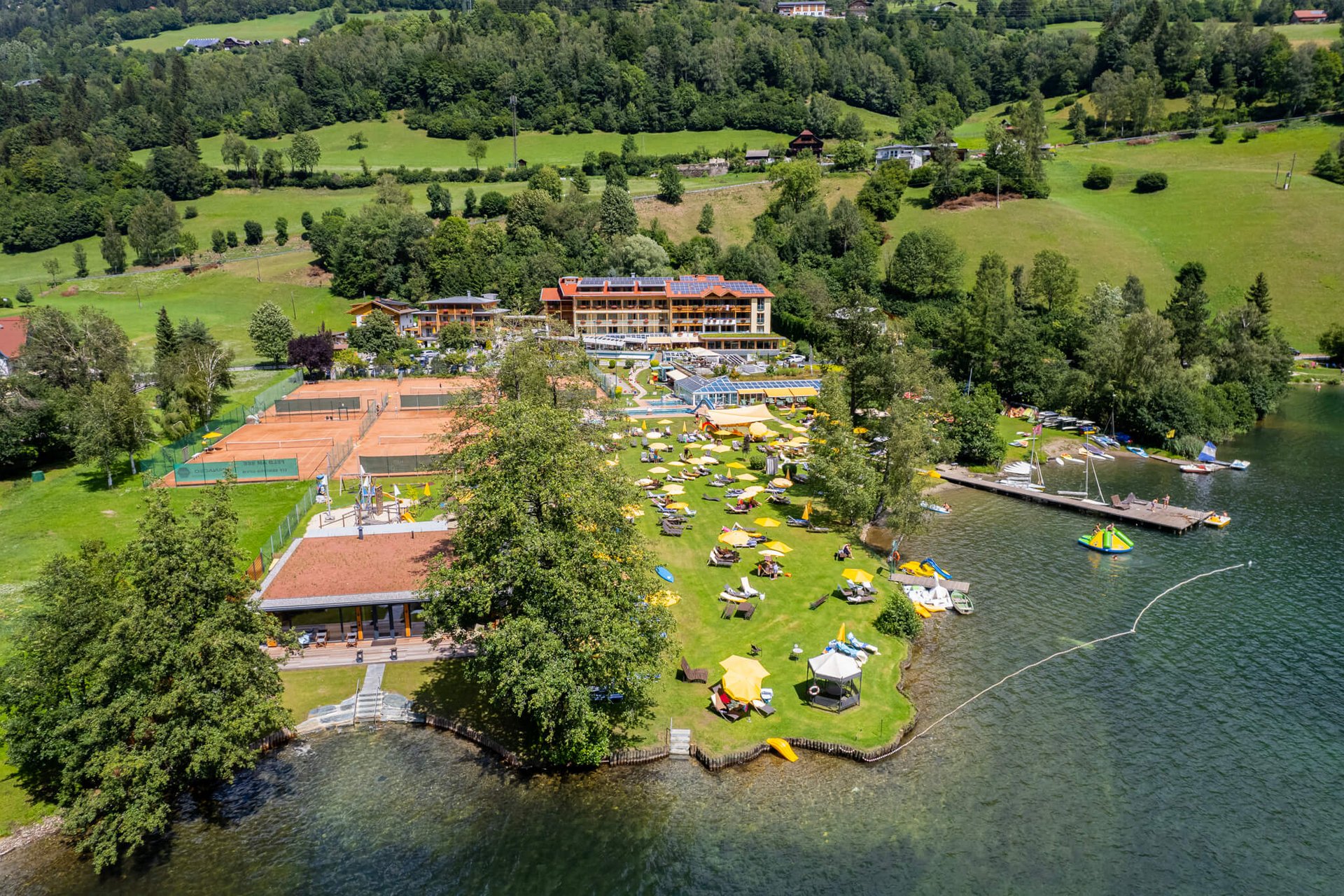 Ansicht eines Seeresorts mit Liegewiese, Tennisplätzen und Bootsanlegestelle