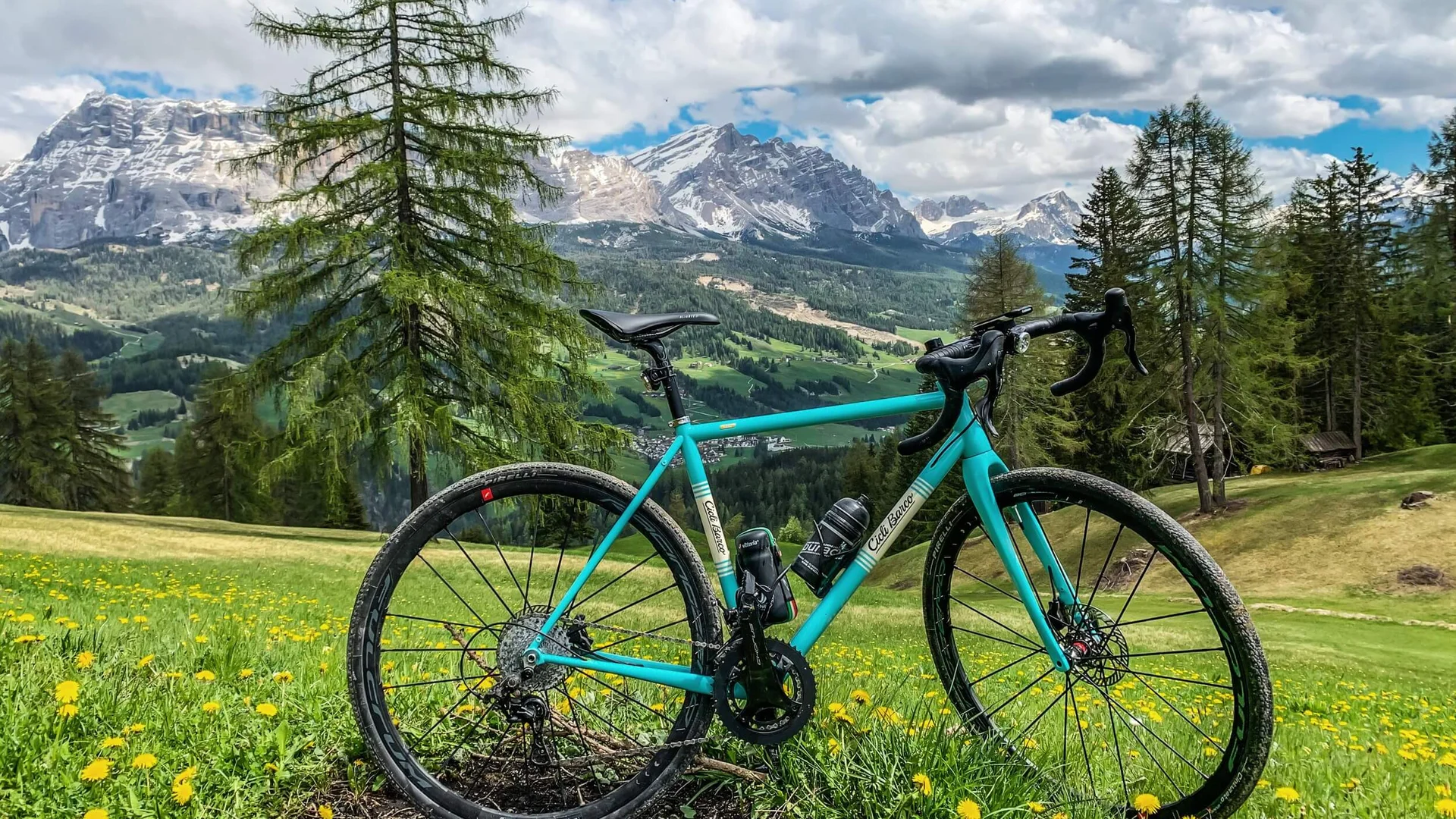 Gravel & Genuss am Kronplatz © Hotel Ostaria Posta Fahrrad auf grüner Wiese vor Bergen und bewölktem Himmel
