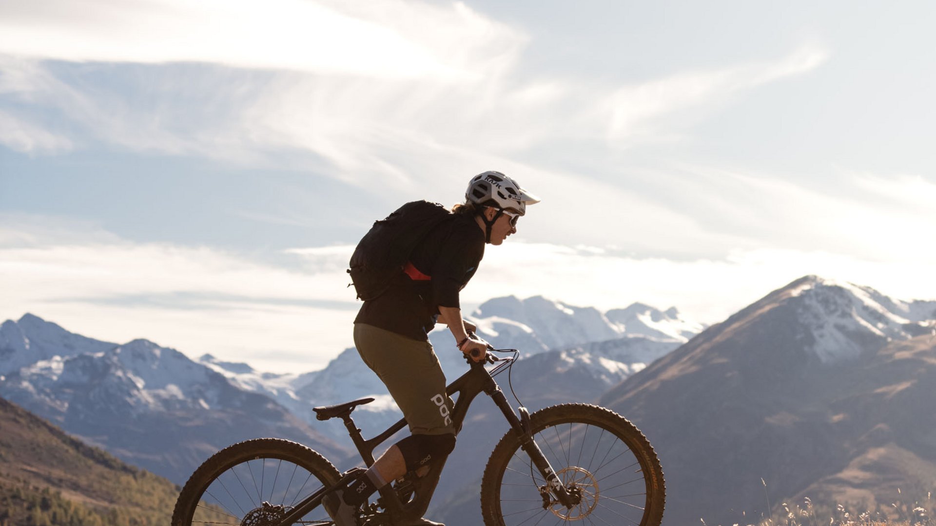 Mountainbiker fährt auf einem Hügel mit Bergpanorama bei klarem Himmel