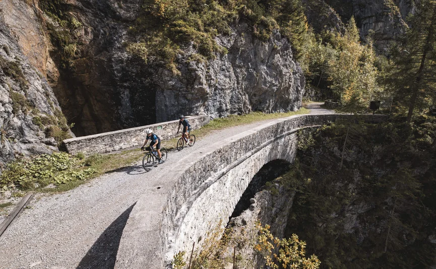 Zwei Radfahrer auf einer Steinbrücke in bergiger Landschaft