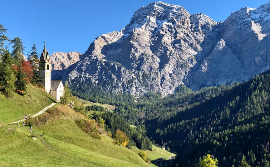 Kirche auf grünem Hügel mit Bergen im Hintergrund bei klarem Himmel