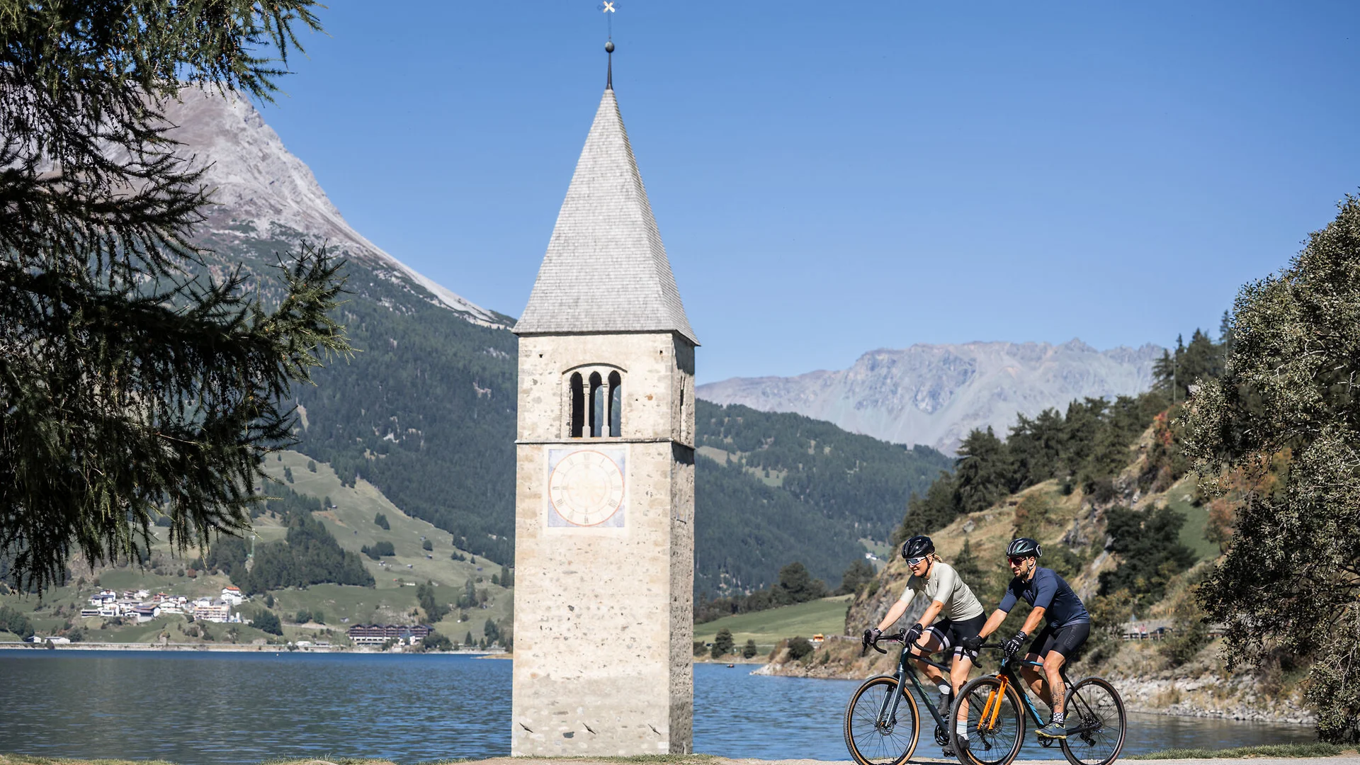 Ein Gravel-Wochenende in Nauders-Reschensee © Heiko Mandl Zwei Radfahrer neben Turm im See mit Berglandschaft im Hintergrund