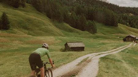 Cyclist riding on gravel path through green mountainous landscape under blue sky