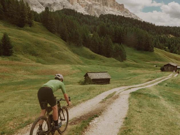 Cyclist riding on gravel path through green mountainous landscape under blue sky