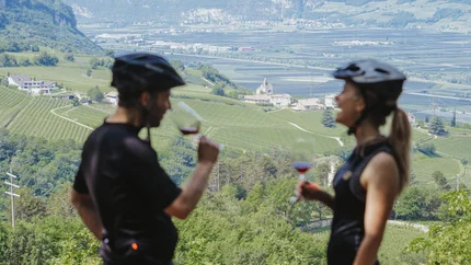 Fünf Dinge, die einen Gravelbike-Urlaub in Südtirols Süden besonders machen © Thomas Monsorno - TV Castelfeder Zwei Radfahrer genießen Wein mit Aussicht auf grüne Weinberge und Berge