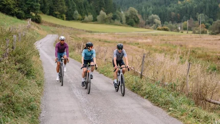 Drei Radfahrer fahren auf einem Landweg durch eine bewaldete Berglandschaft